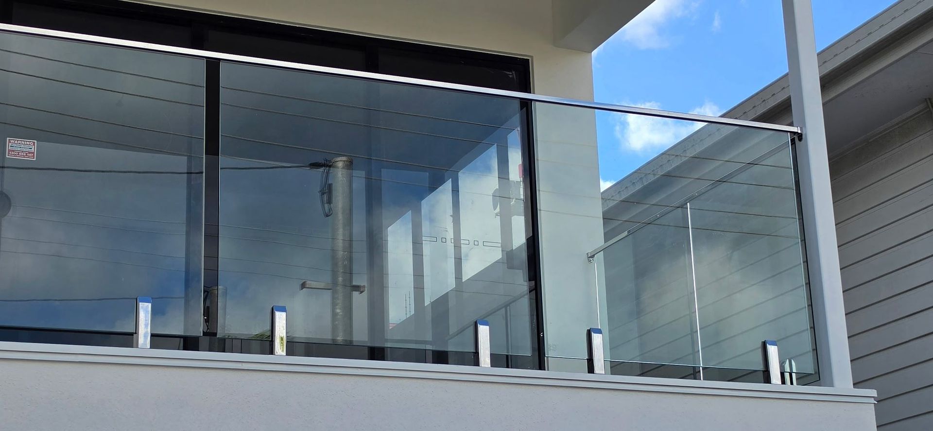 Modern balcony with glass railing, white walls, and blue sky reflected in the windows