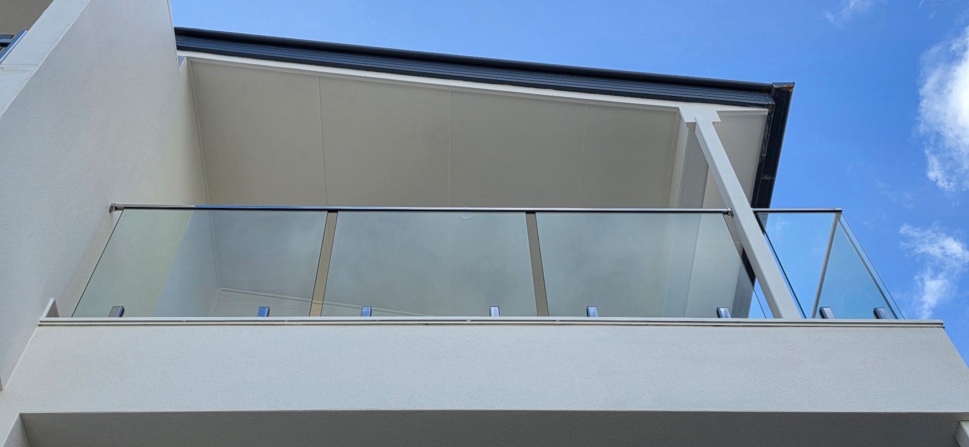 Modern apartment balcony with glass railing against a blue sky