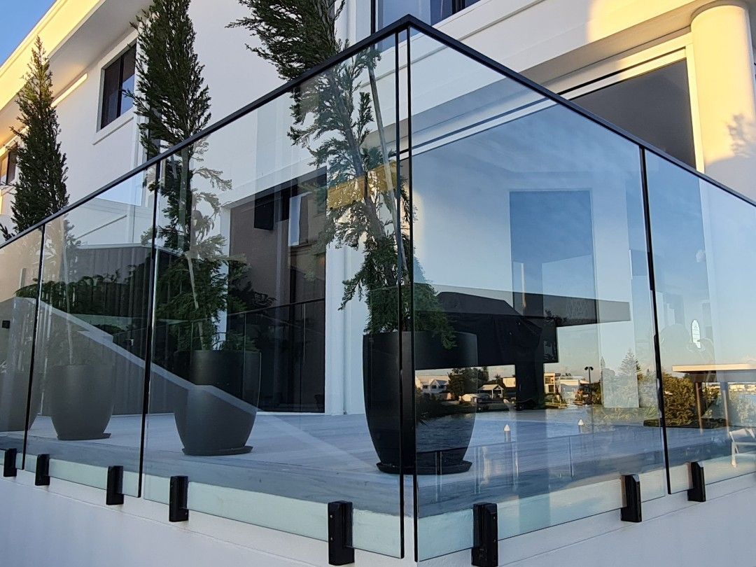 Glass balcony railing with black posts on a modern home, potted plants and deck.