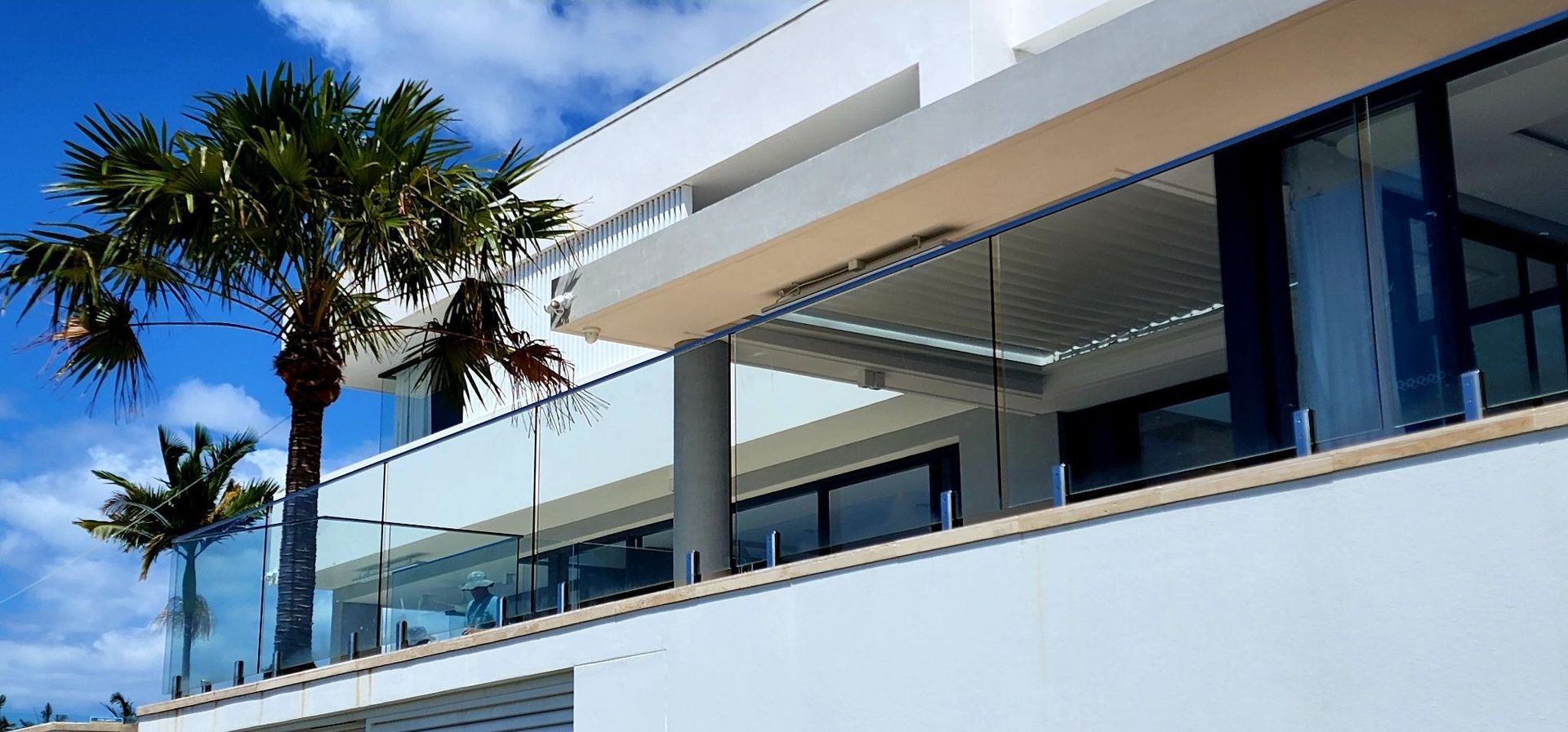 Modern white building with palm trees, blue sky.