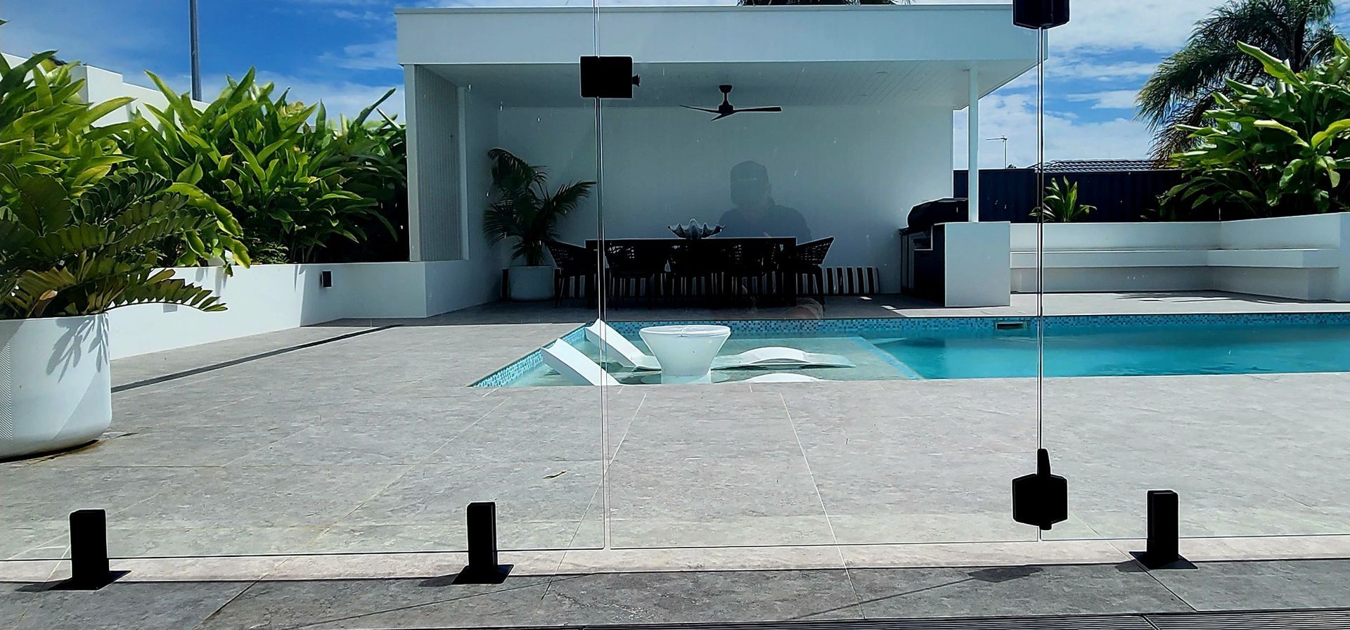 A patio with a pool and outdoor seating area, white architecture, and lush green plants.