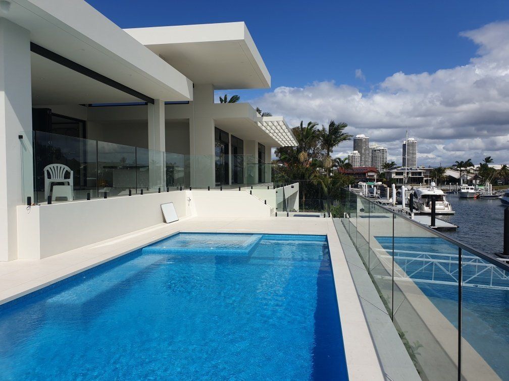Luxurious white house with a pool by the water; sunny day.