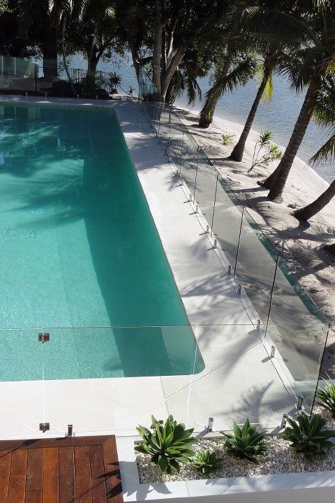 Swimming pool next to a beach with clear glass fencing and palm trees.