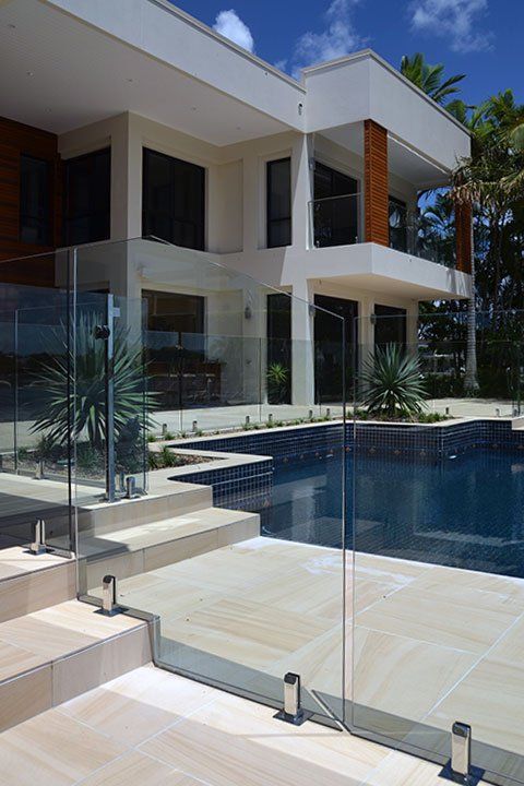 Modern house with a pool. Glass railing, tiled steps, blue pool water, and a two-story building with large windows.
