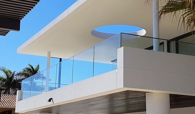 Modern white building with glass balcony, clear blue sky, palm trees.