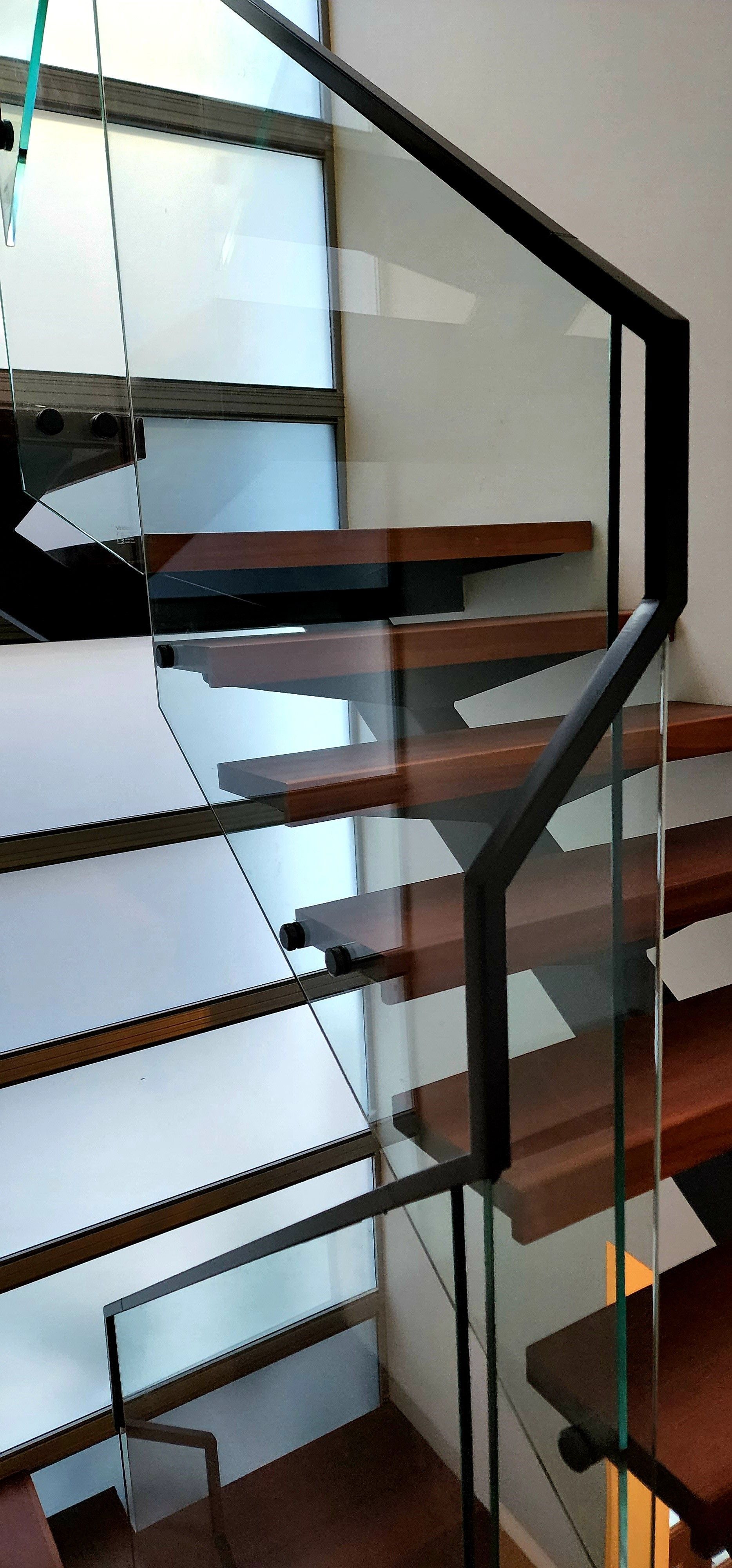 Wooden staircase with glass railings and black metal supports.