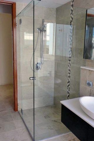 Glass shower enclosure with chrome fixtures against beige tiled walls.