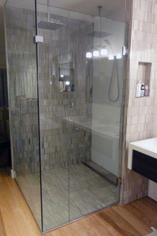 Glass shower enclosure with two showerheads, tile walls, and wooden floor.