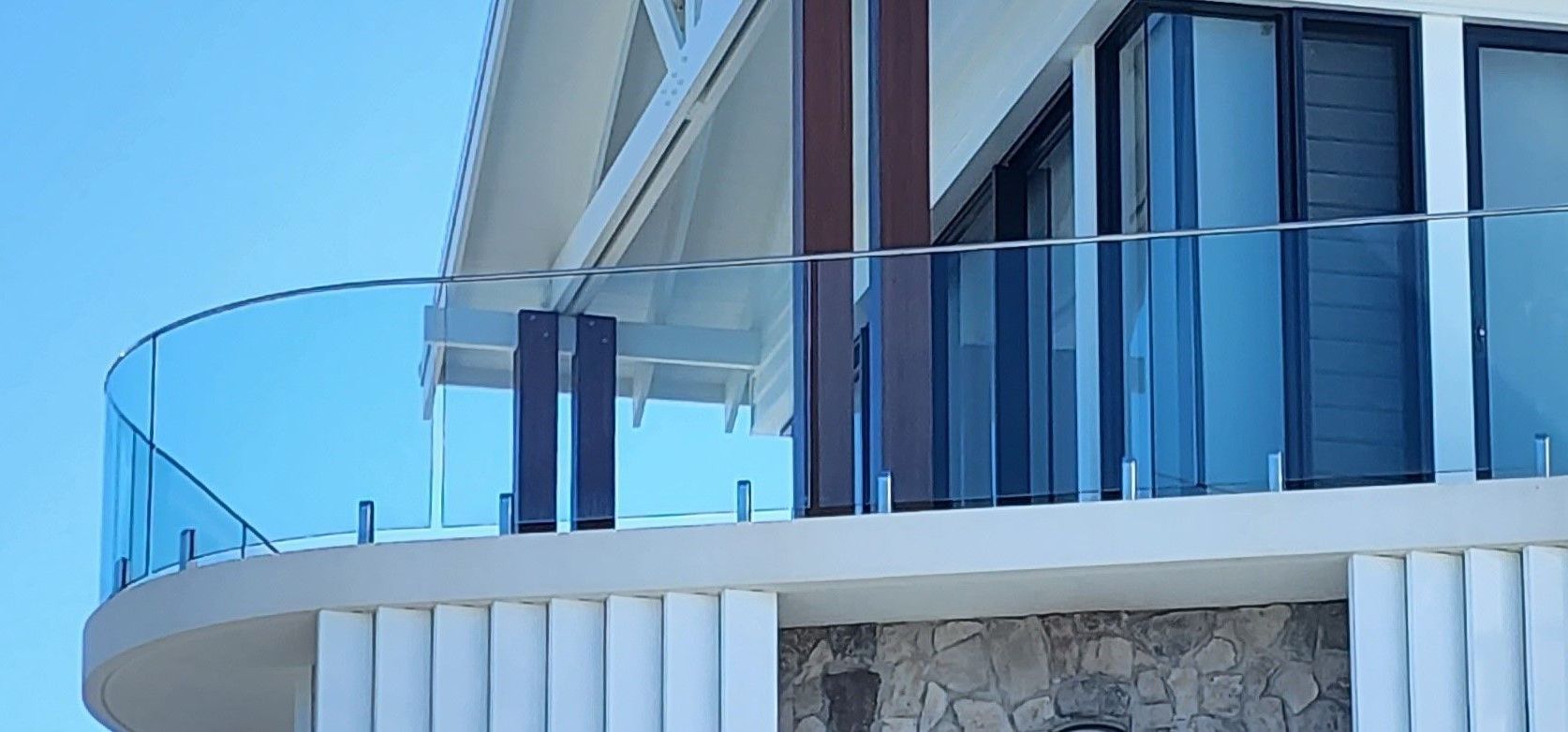 A modern building with a curved glass balcony, blue sky.