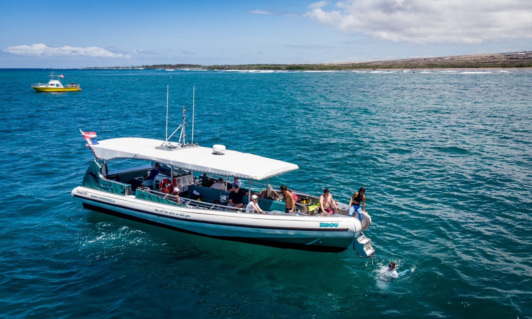 Tour boat with passengers on bright blue water, with a small yellow boat in the distance.