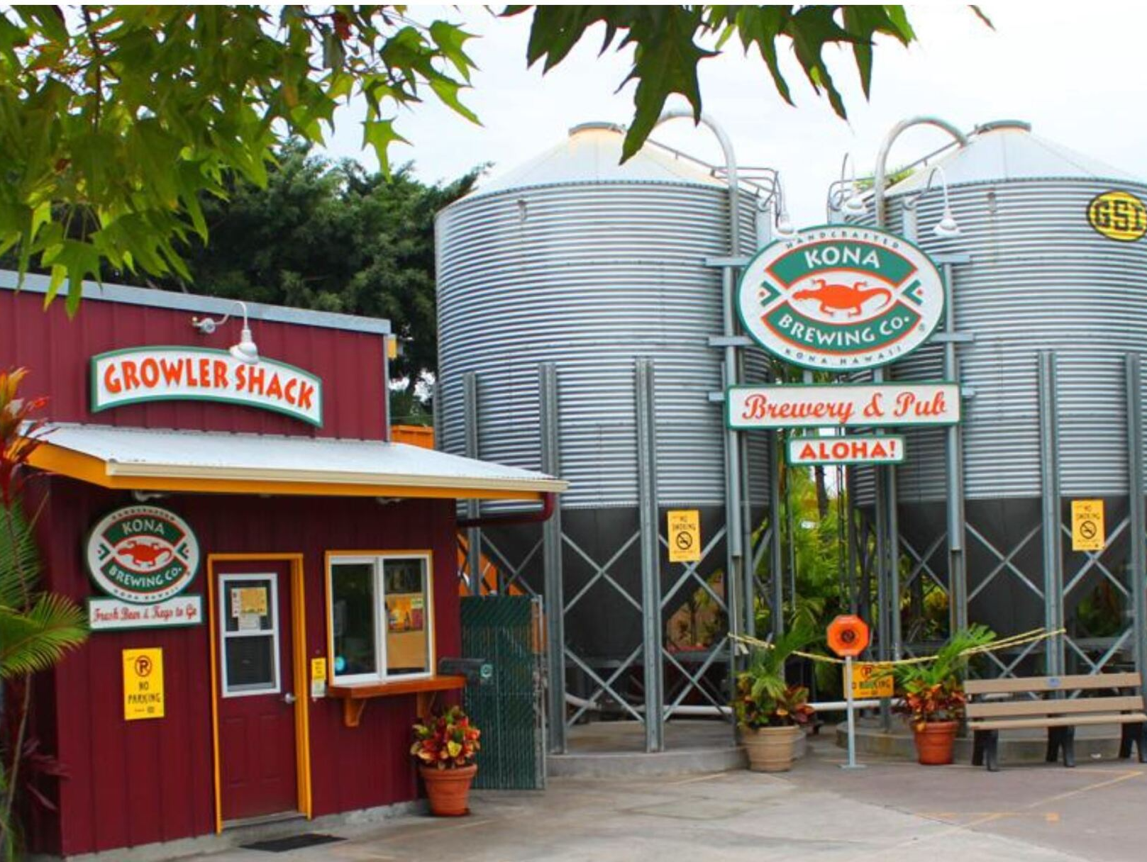 Red growler shack beside large metal tanks with a “Brewery & Pub” sign and potted flowers