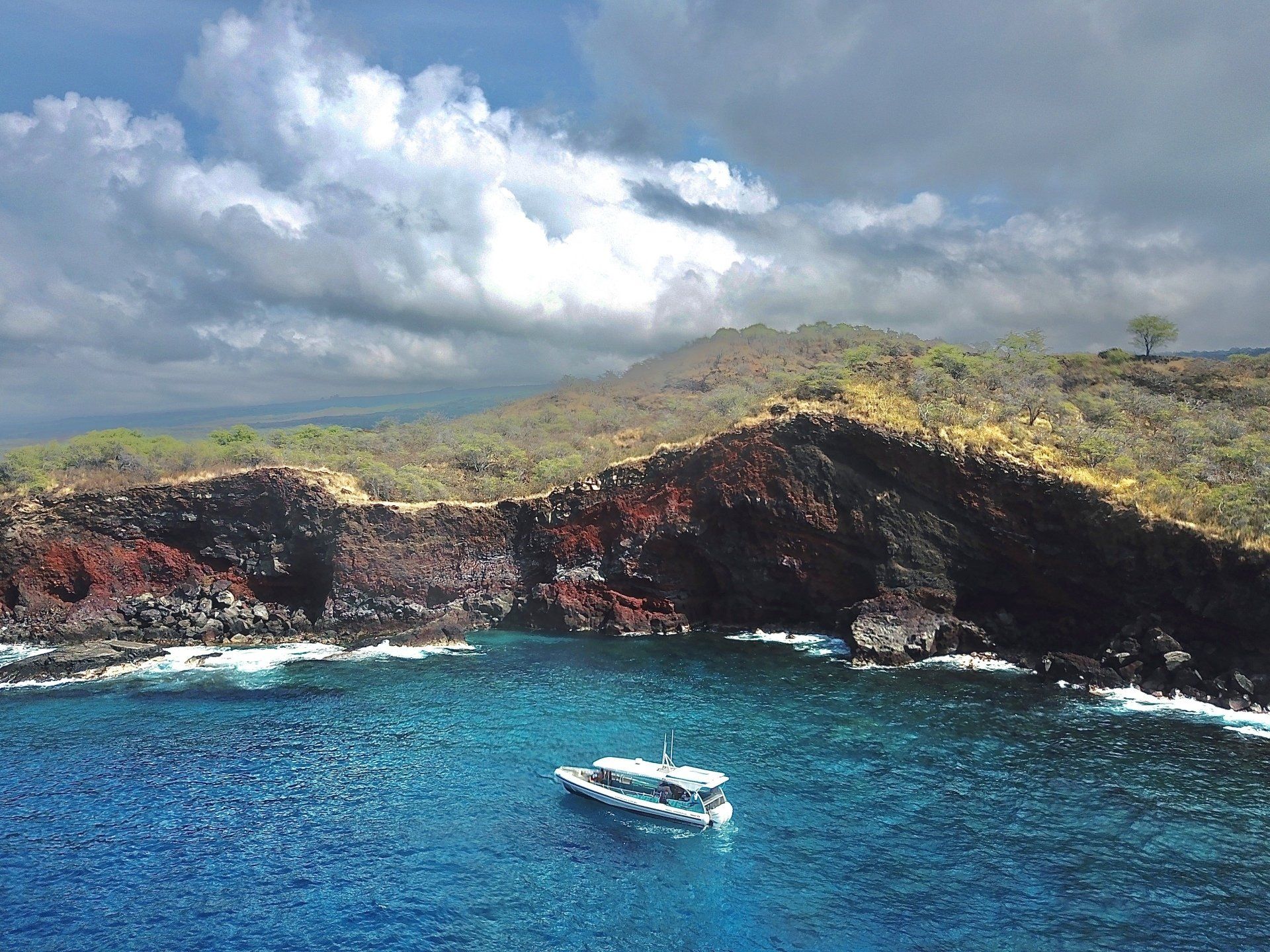 Tour boat on turquoise water below rugged volcanic cliffs under cloudy sky