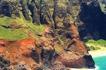 Steep green and rust-colored sea cliffs above a turquoise shoreline and small sandy cove