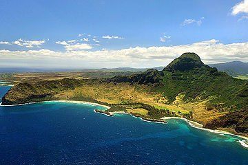 Tropical coastline with blue ocean, sandy beach, and lush green mountains under a partly cloudy sky