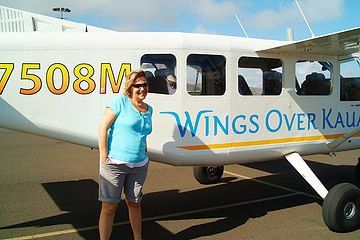Woman standing beside a small white airplane with “Wings Over Kauai” on the side.