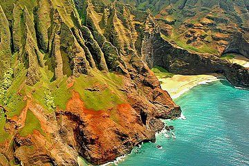 Steep green and orange sea cliffs beside a turquoise cove and sandy beach