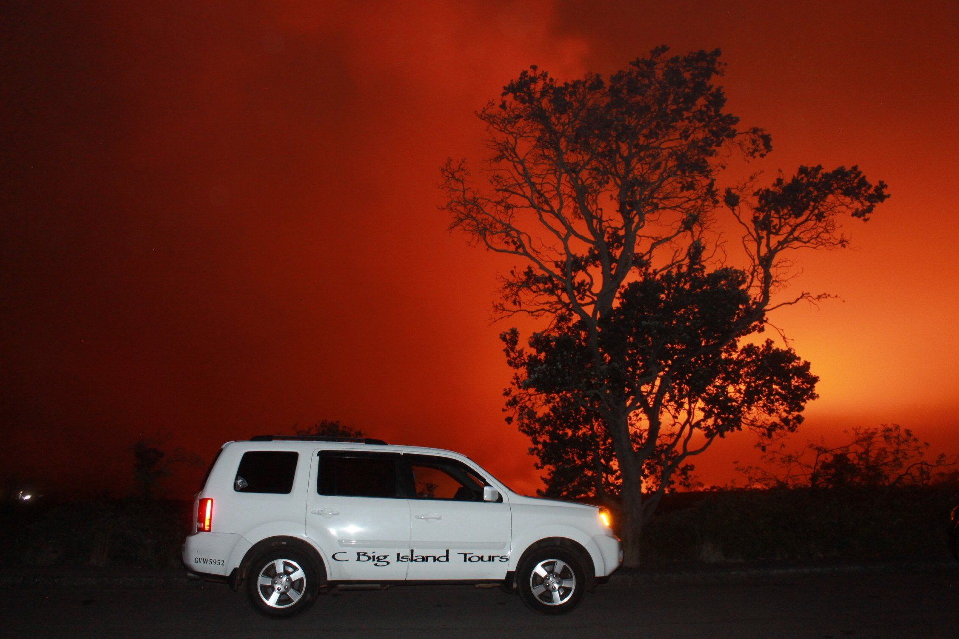 White SUV parked at night before a tree silhouetted against a bright orange wildfire glow
