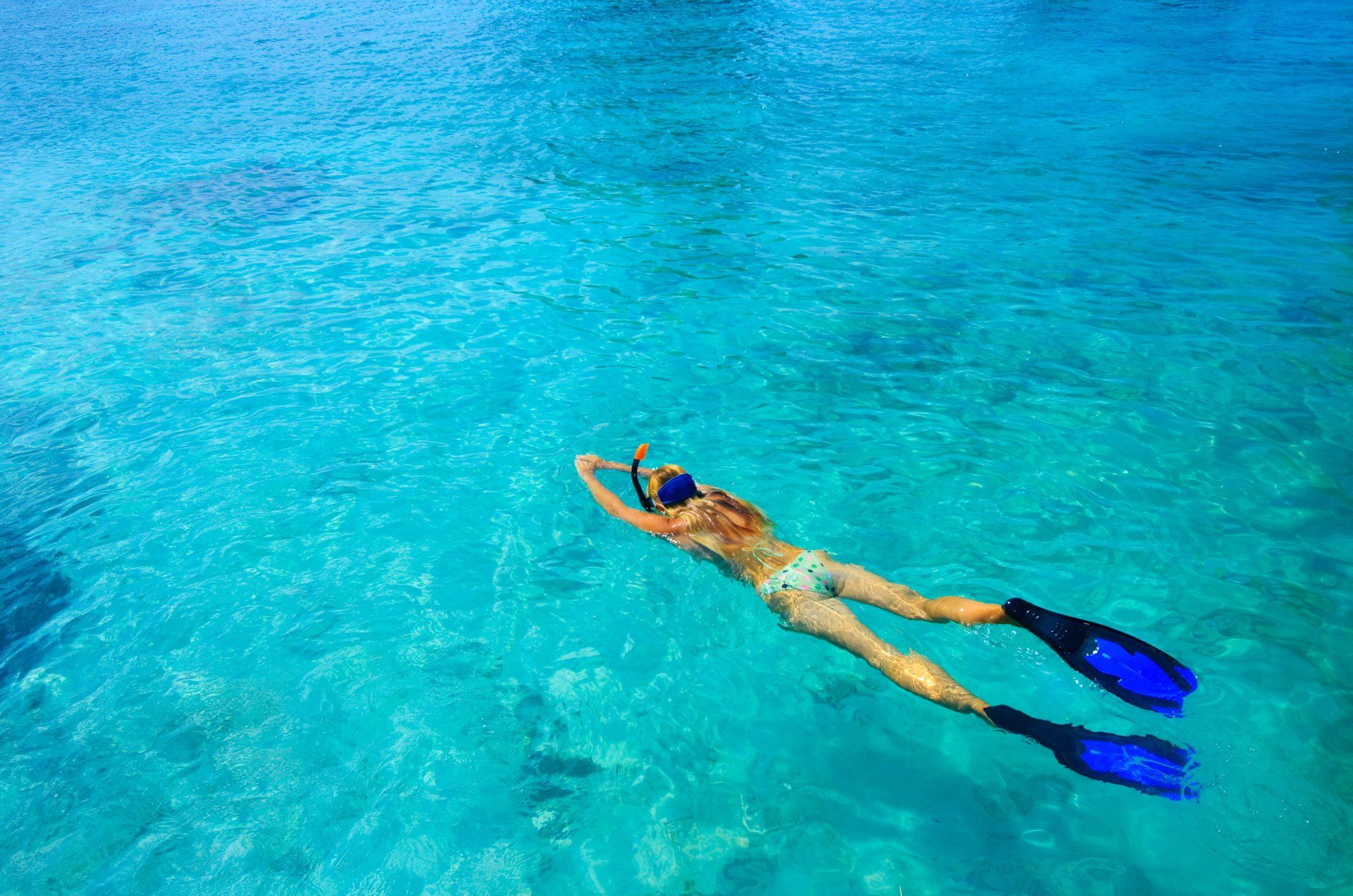 Person snorkeling in clear turquoise water with blue fins