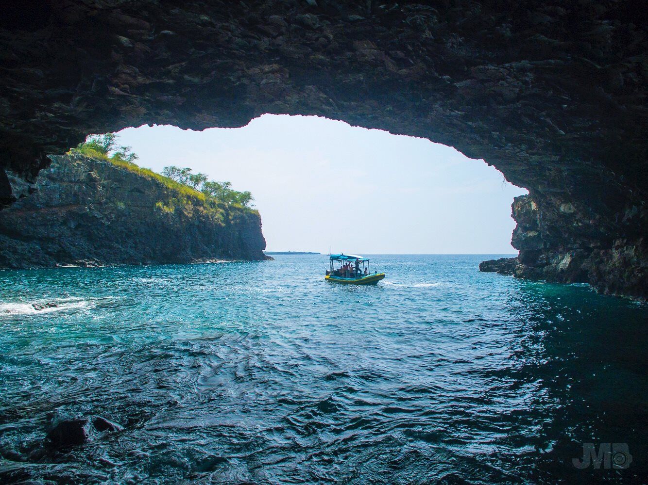 Boat in a turquoise sea framed by a rocky cave opening, with bright sky beyond.