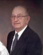 Studio portrait of an older man in a dark suit, white shirt, and tie, facing the camera.