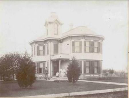 Old two-story Victorian house with a porch, bay windows, and a front lawn.