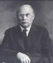 Black-and-white portrait of a man in a dark suit, seated with a serious expression.