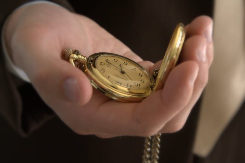 A hand holds an open gold pocket watch with a chain attached.