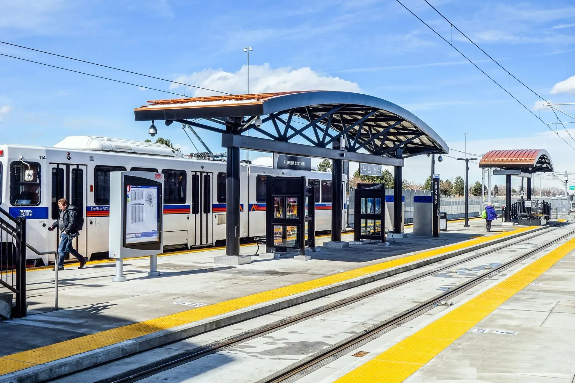 Modern train station platform with a white and blue train, shelters, and tracks under a clear sky