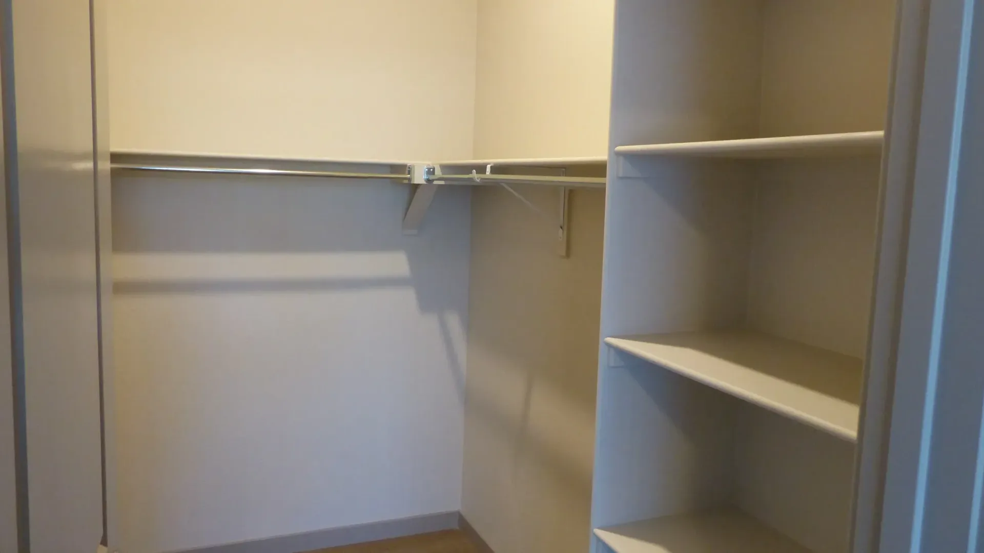 Empty walk-in closet with white shelves, hanging rods, and beige carpet.