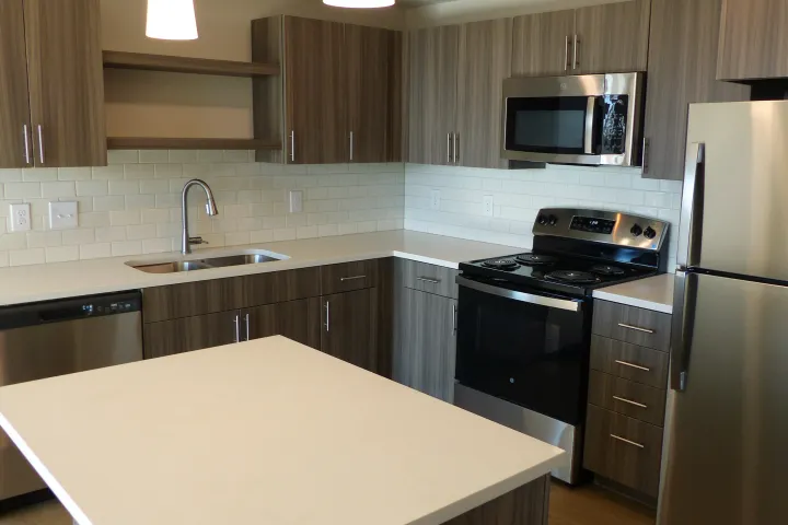 Modern kitchen with wood cabinets, white countertops, stainless appliances, and a central island