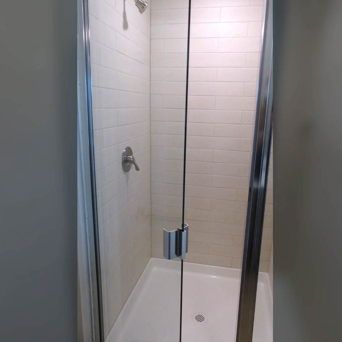 Small shower stall with white tiled walls, a showerhead, and a frosted glass door.