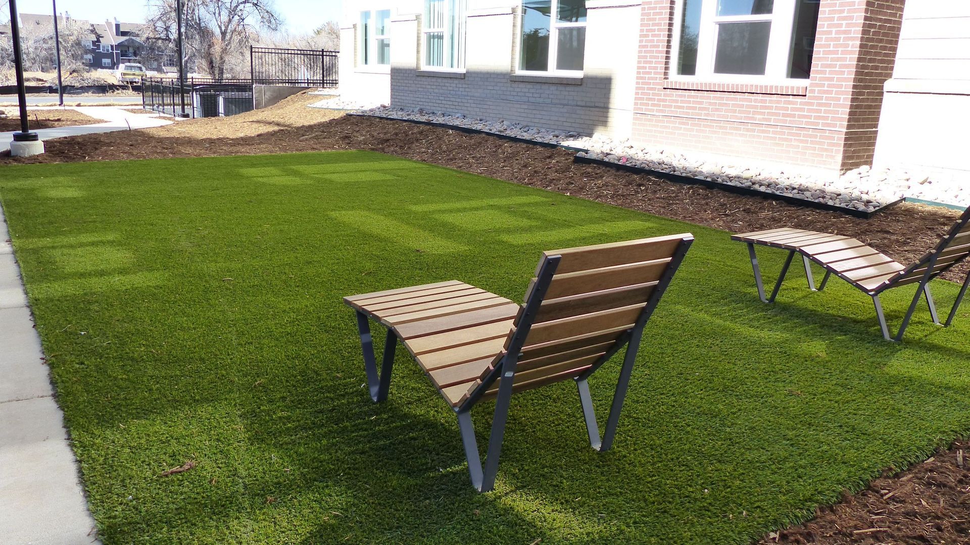 Two wooden chairs on a small artificial grass patio beside a house.