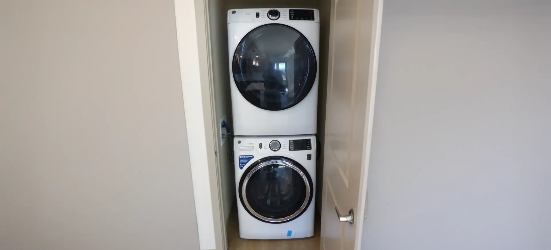 Stacked washer and dryer in a narrow closet, with front-loading machines visible.