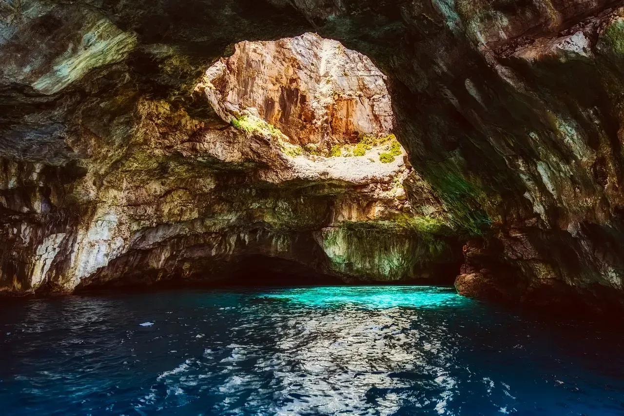 Rocky sea cave opening to turquoise water with sunlight streaming in