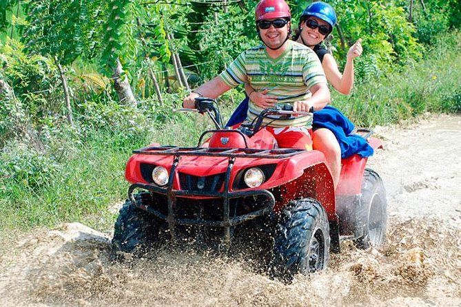 Two people riding a red ATV through muddy water on a forest trail in puerto plata