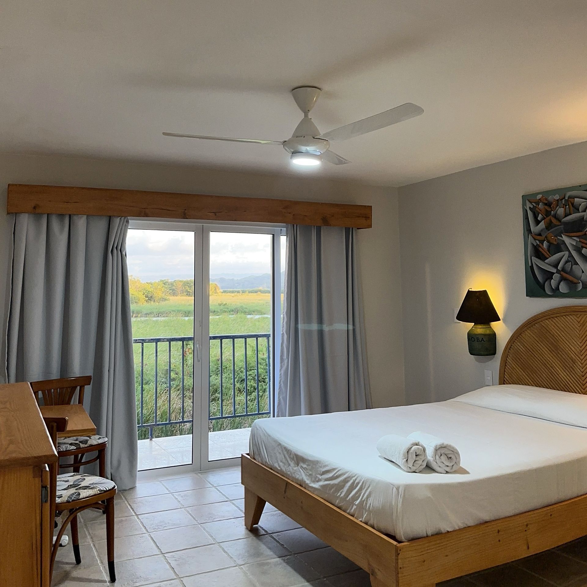 Bright bedroom with a bed, balcony doors, and a view of green fields outside.