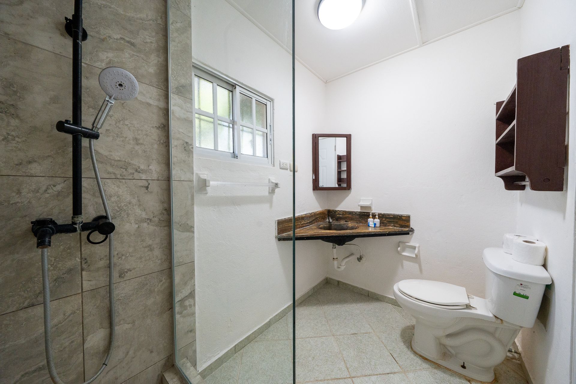 Accessible bathroom with walk-in shower, wall-mounted sink, toilet, and grab bars on tiled walls