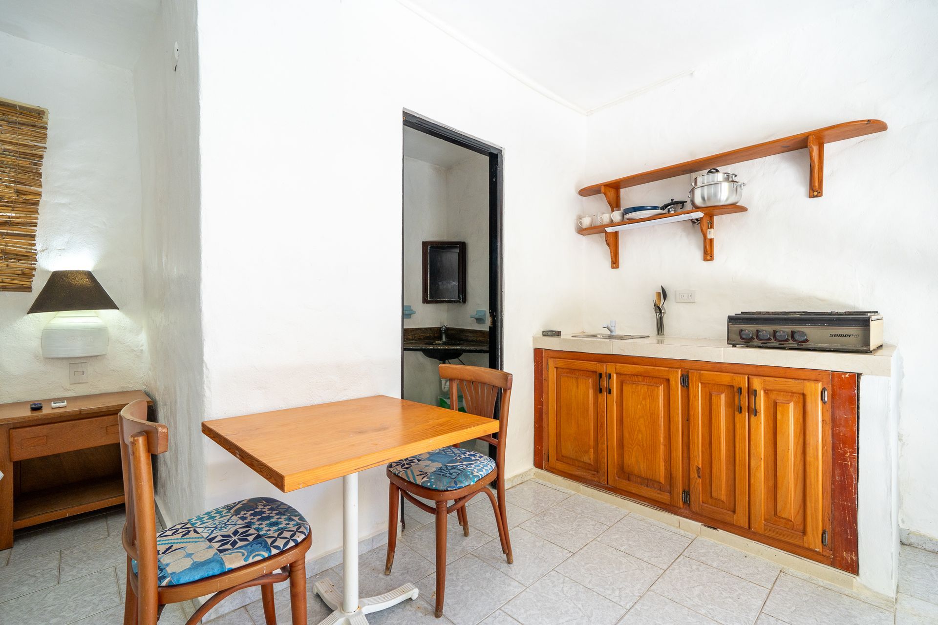 Small dining area with wooden table, chairs, sideboard, and wall shelves in a bright room