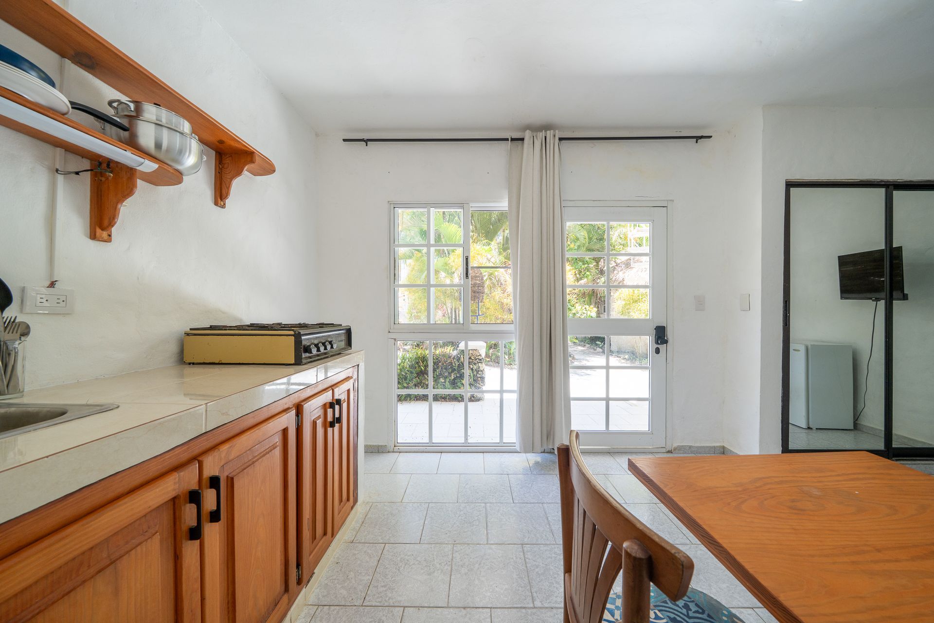 Bright kitchen with wooden cabinets, white tile floor, and glass doors leading outside.