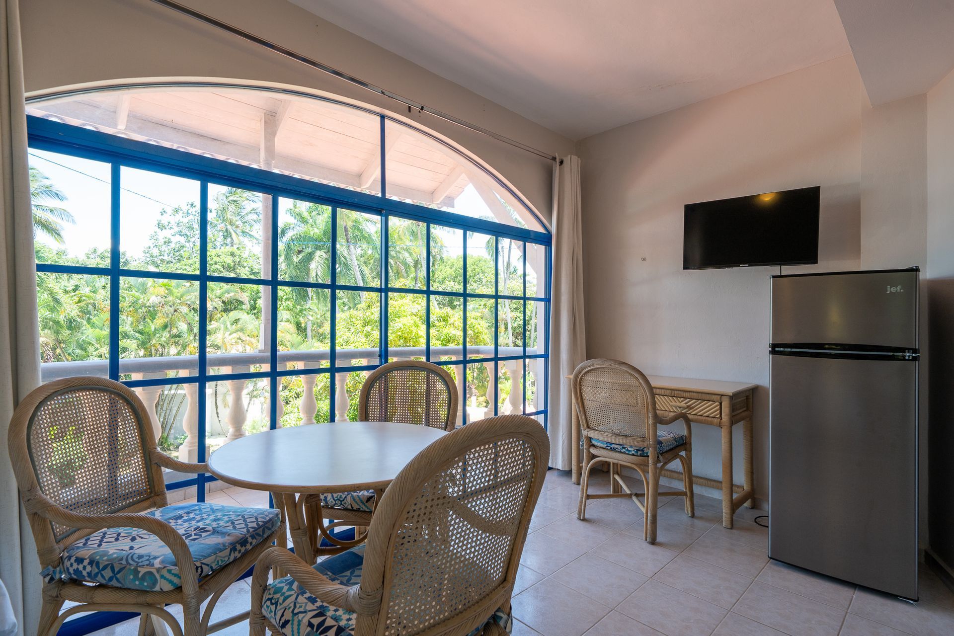 Bright sunroom with round table, wicker chairs, large arched windows, TV, and mini fridge