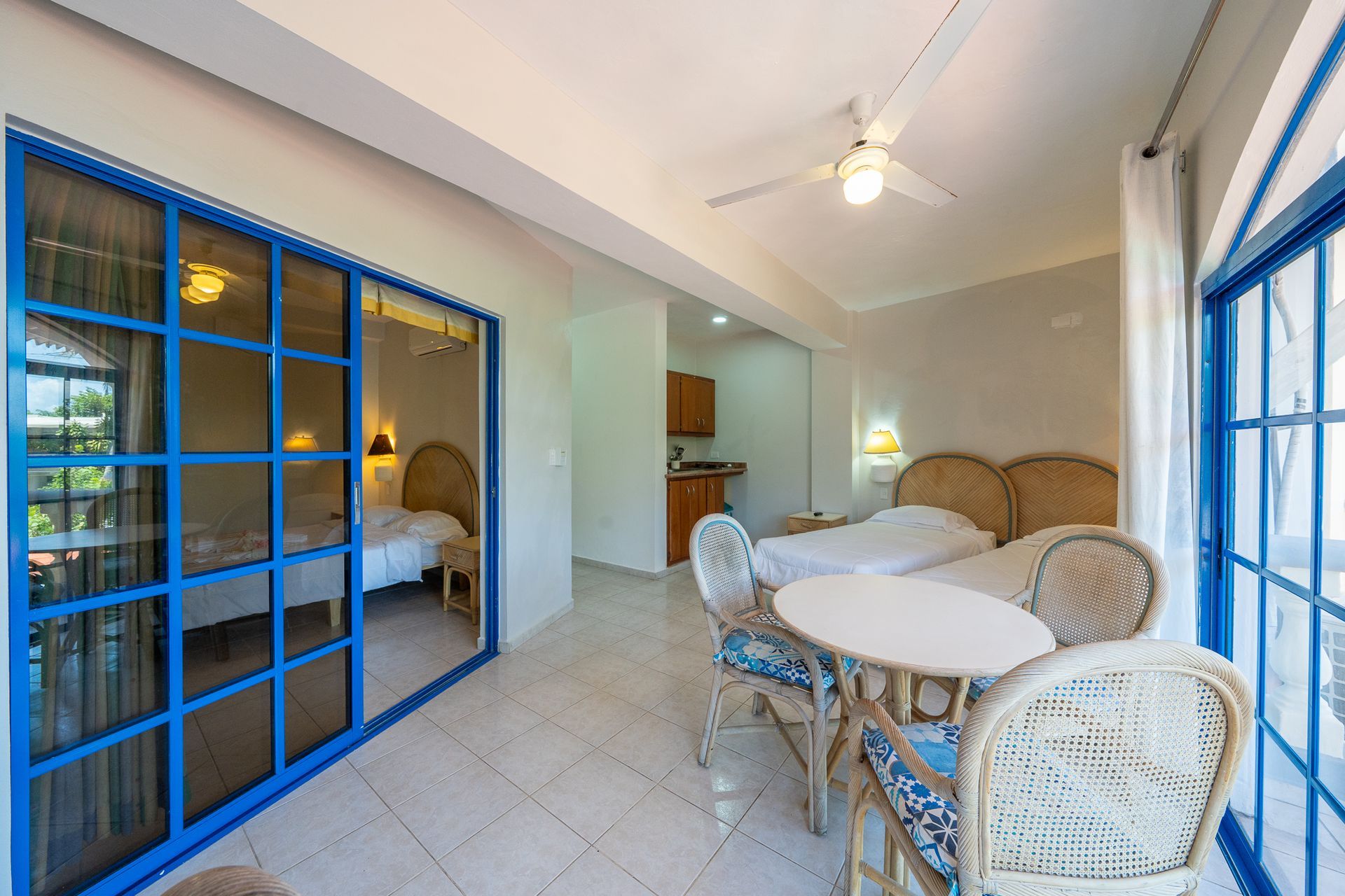 Bright sunroom with wicker dining set, blue-trimmed sliding doors, and a view into a bedroom.