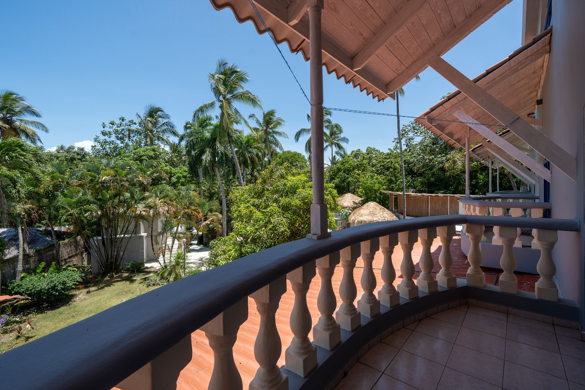 Shaded balcony overlooking a lush tropical garden with palm trees and terracotta tiles