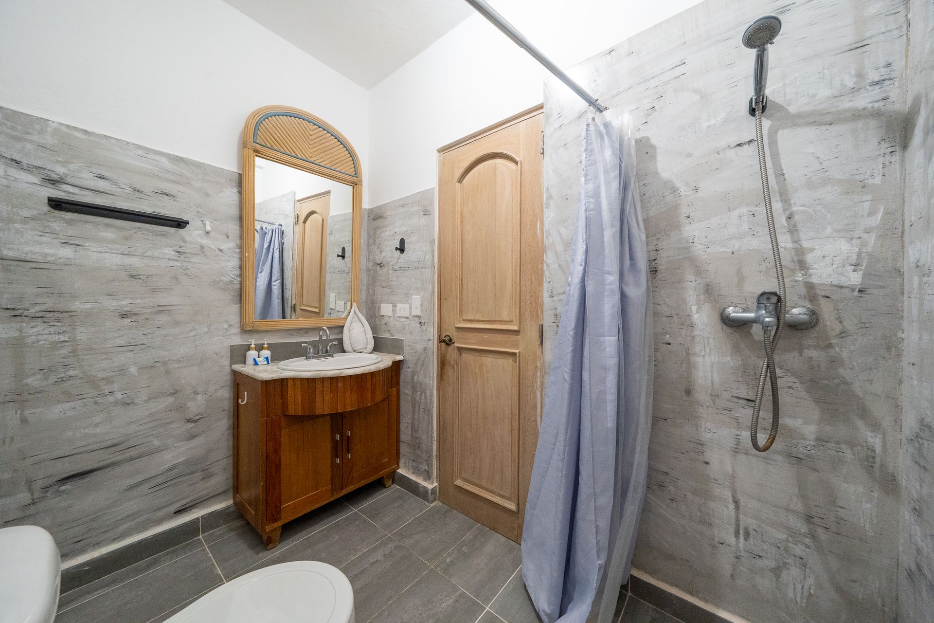 Small tiled bathroom with wood vanity, mirror, shower, and a closed door.