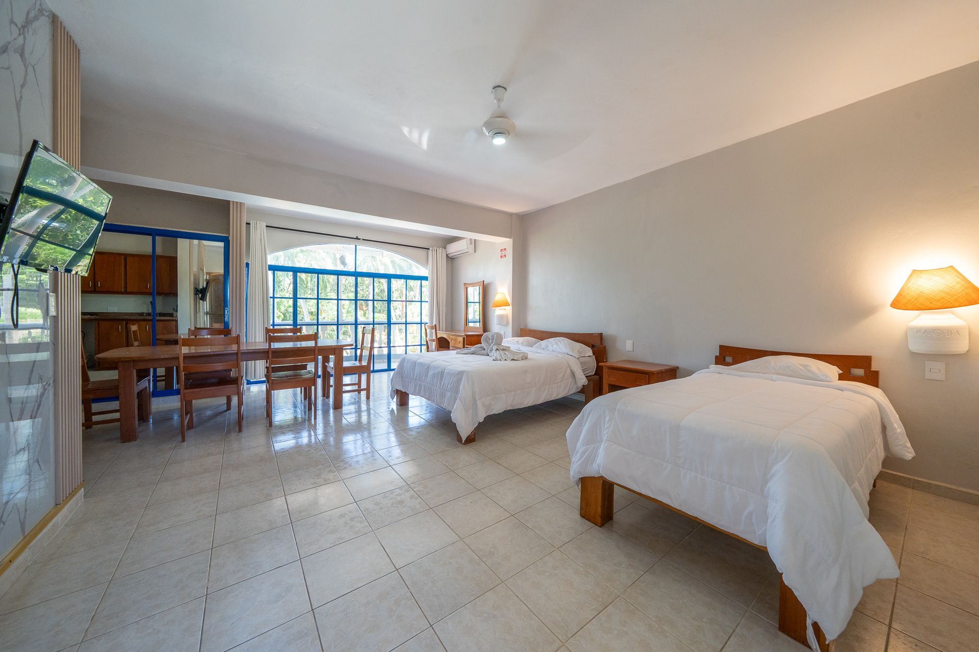 Spacious hotel room with two beds, tiled floor, dining area, and sliding glass doors to a balcony