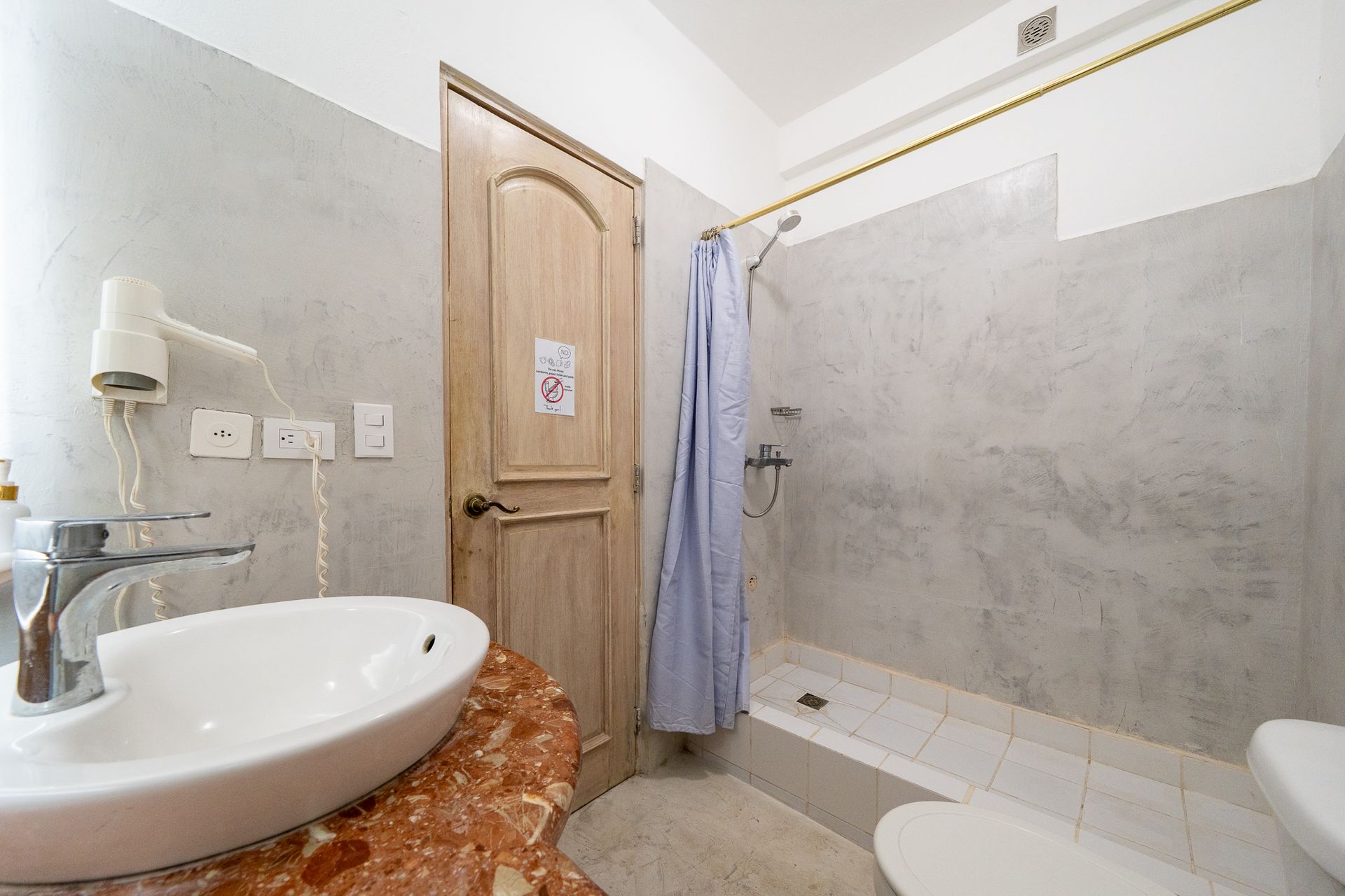 Small bathroom with a sink, shower curtain, bathtub, and wooden door.