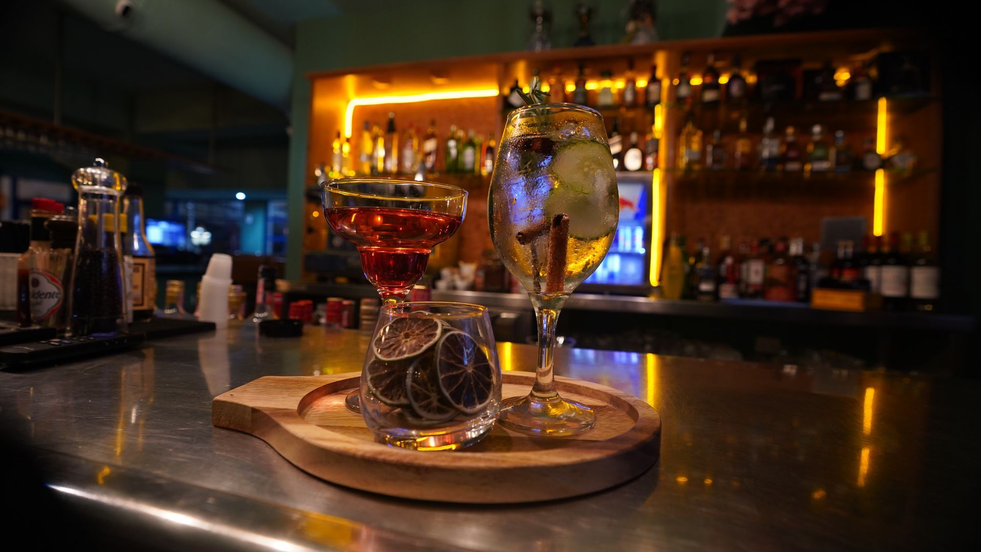 Cocktail glass on a tray at a warmly lit bar counter, with bottles glowing in the background