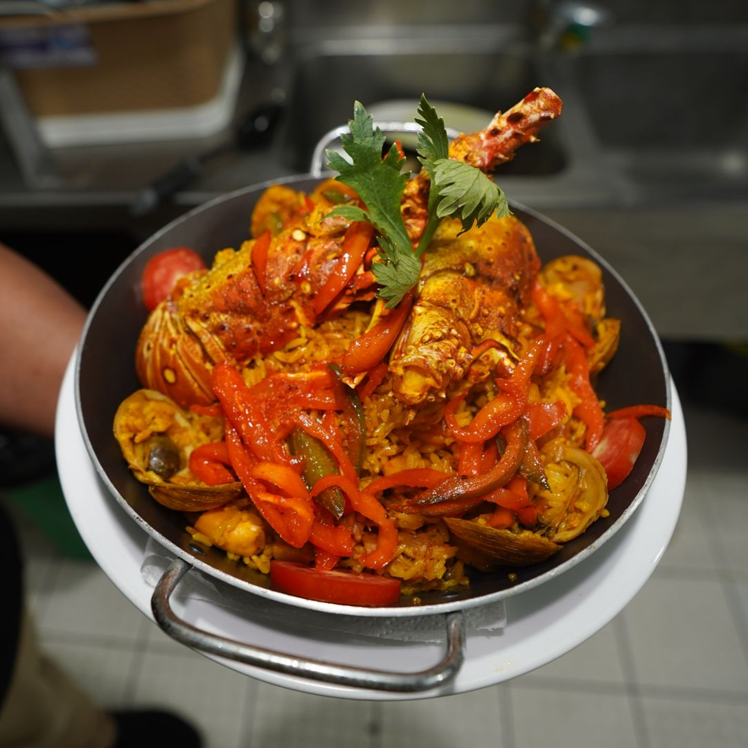 Bowl of spicy seafood curry with red peppers and cilantro, served on a metal tray in a kitchen