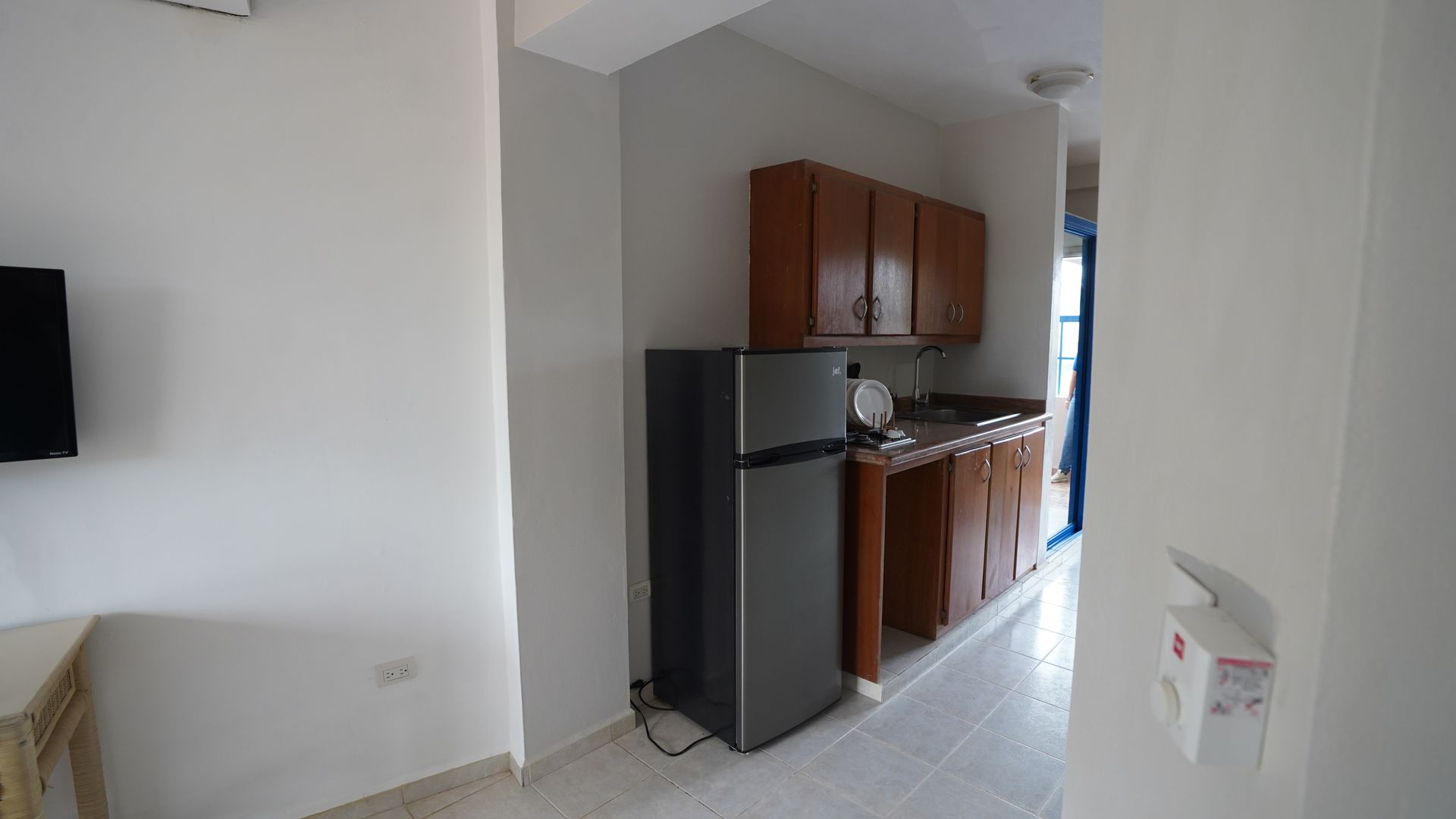 Small kitchen with dark refrigerator, wooden cabinets, and a countertop in a bright apartment interior.