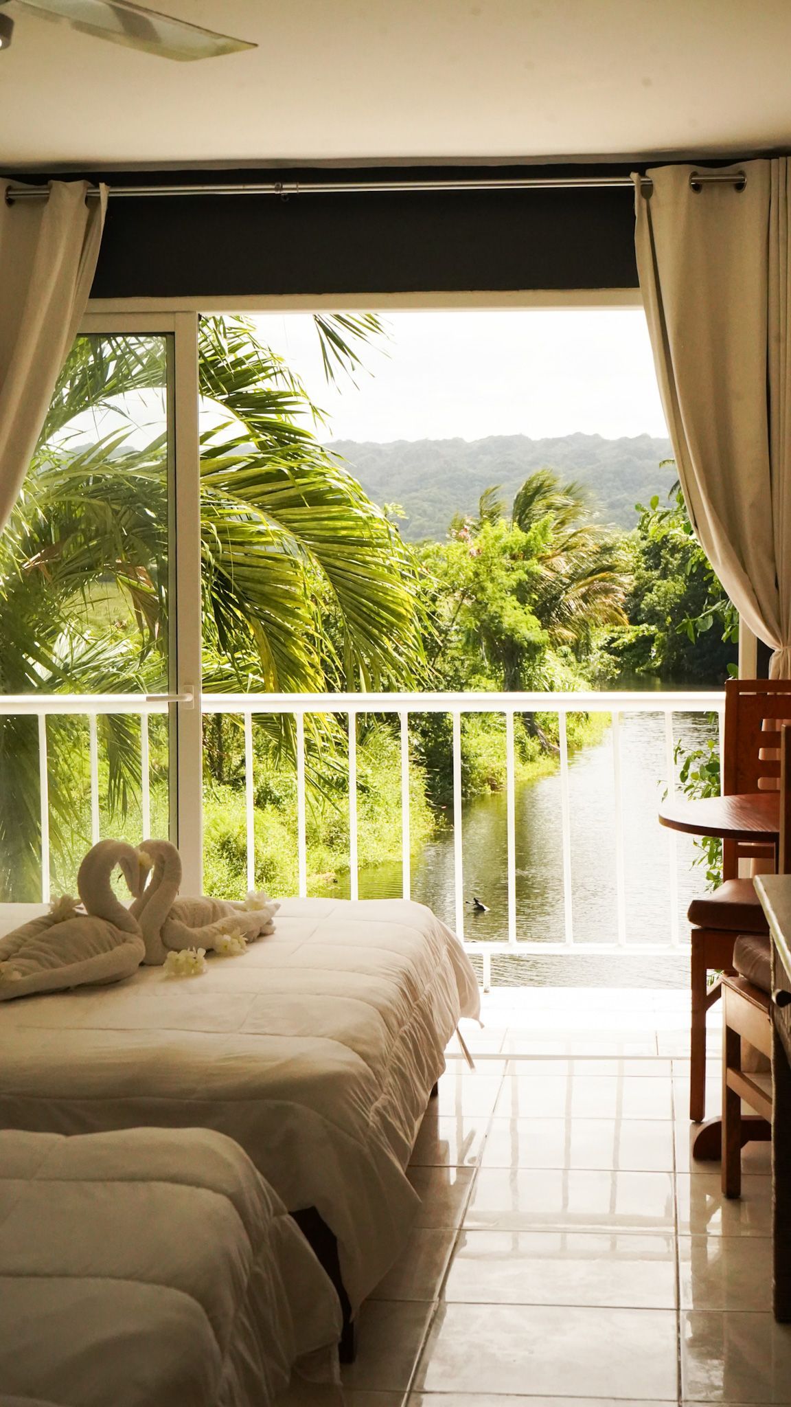 Bedroom with twin beds, open balcony doors, and a view of lush green hills outside.