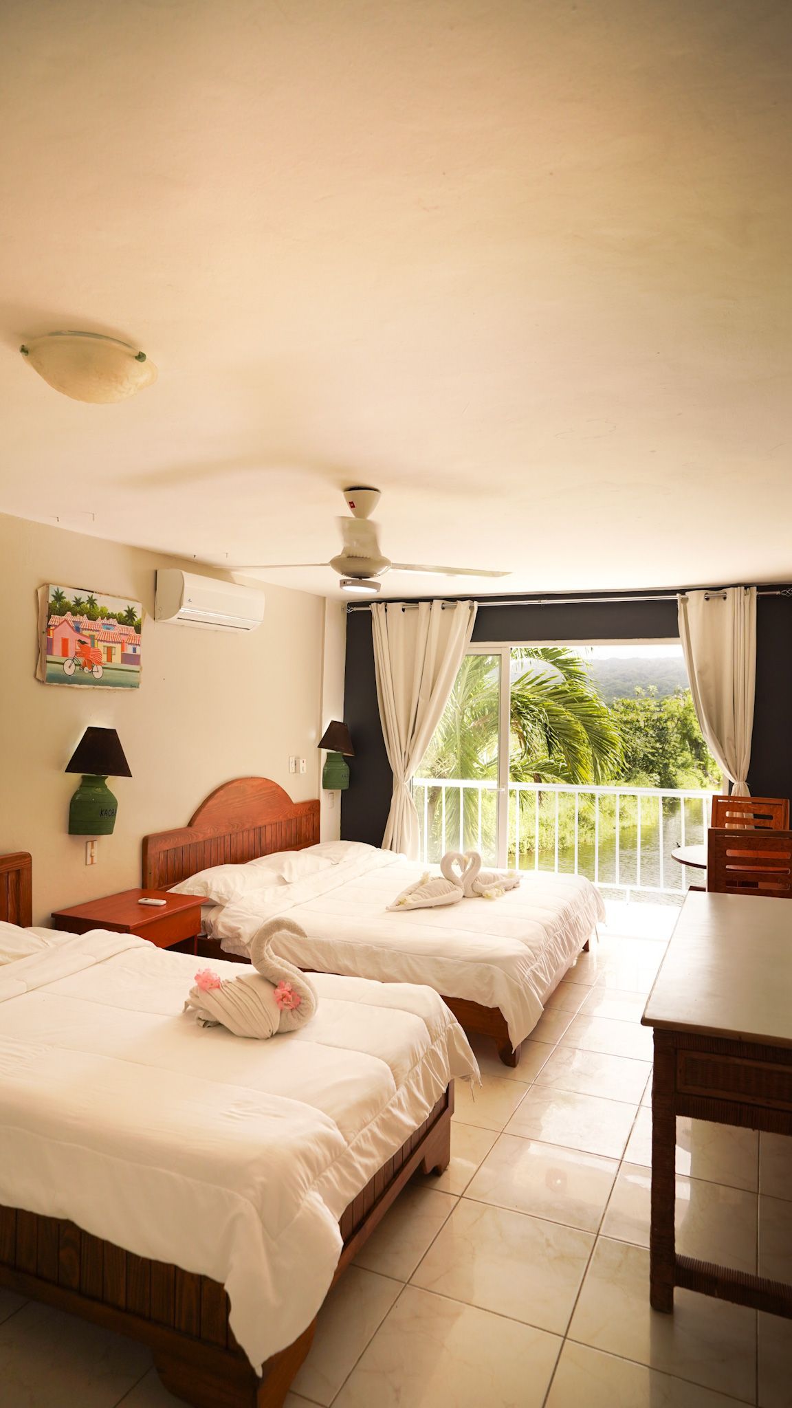 Bright bedroom with two twin beds, white walls, and a balcony view through open curtains.